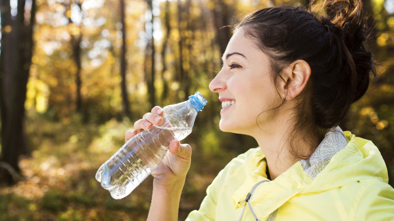 young woman with brown hair in a yellow jacket drinking a bottle of water