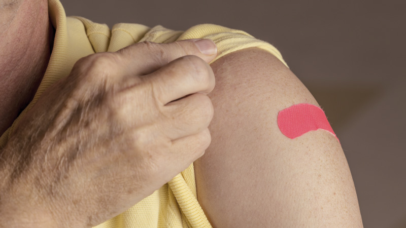 close up of person in yellow shirt with a pink bandage on upper arm from flu shot