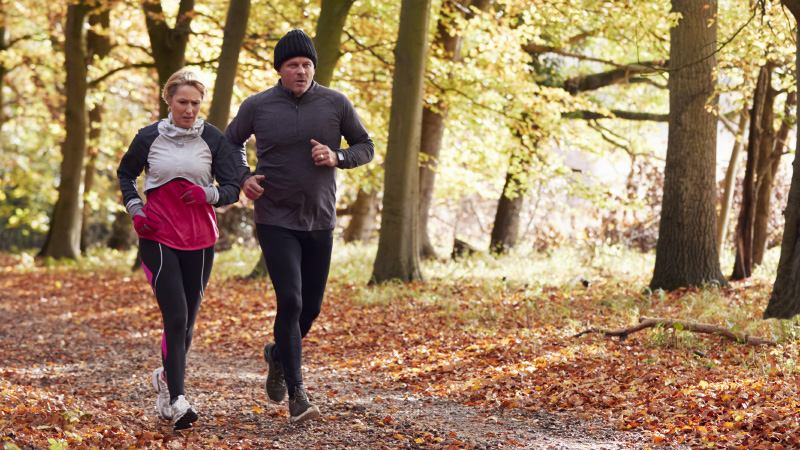 mature couple jogging on a wooded path in the fall