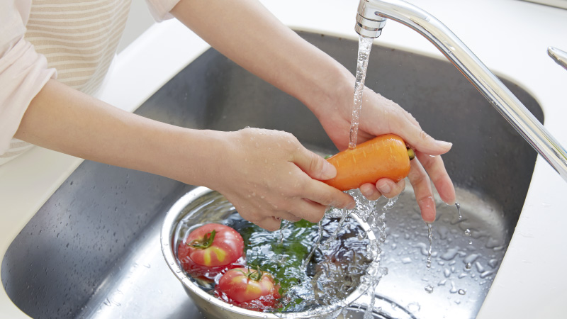 woman's hands washing a carrot and other vegetables in a sink