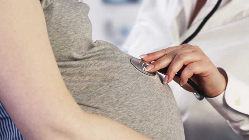 close up of pregnant woman belly while a doctor listens with a stethoscope