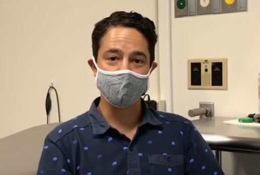 Dr. Borus, wearing a blue button down shirt and a grey mask, looking at camera.