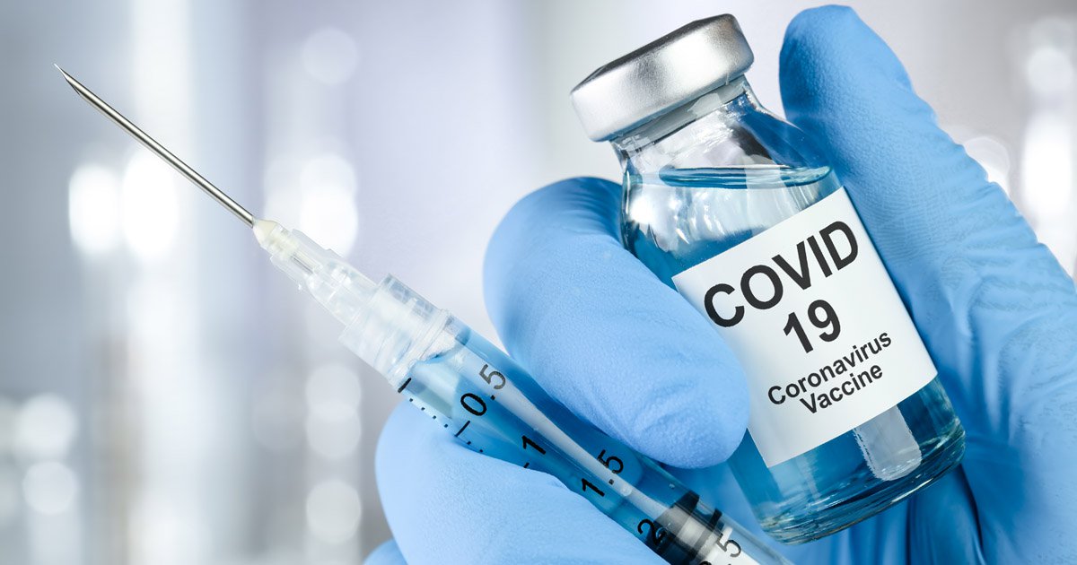 Hand in a blue glove holding a syringe and bottle that says covid 19