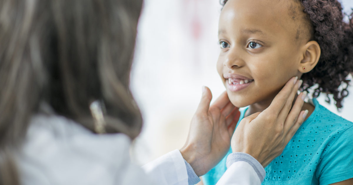 person in white lab coat feeling glands on neck of a child wearing a teal shirt