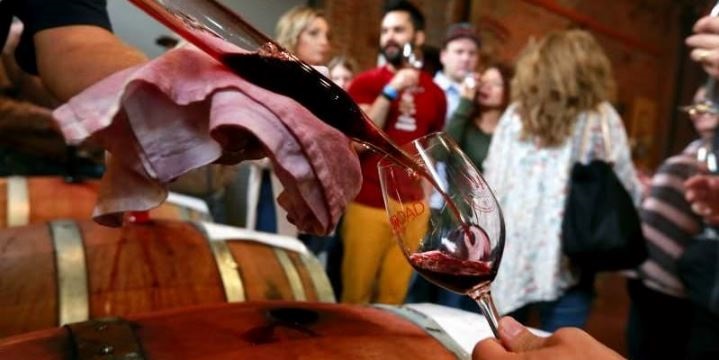 person taking wine out of wine barrels and people in the background talking